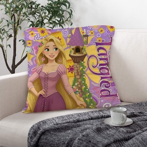May include: Square cushion featuring a cartoon illustration of a princess with long blonde hair, wearing a pink dress. The cushion has a purple and yellow background with the word "Tangled".