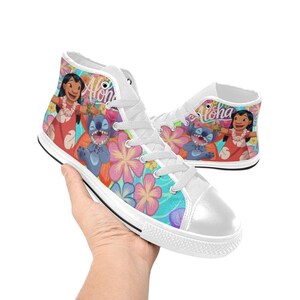 Puede incluir: Zapatillas altas de lona con un dise&ntilde;o floral y de personajes coloridos. Las zapatillas muestran la palabra "Aloha" e im&aacute;genes de Lilo y Stitch. Los zapatos tienen cordones blancos y una suela de goma blanca.