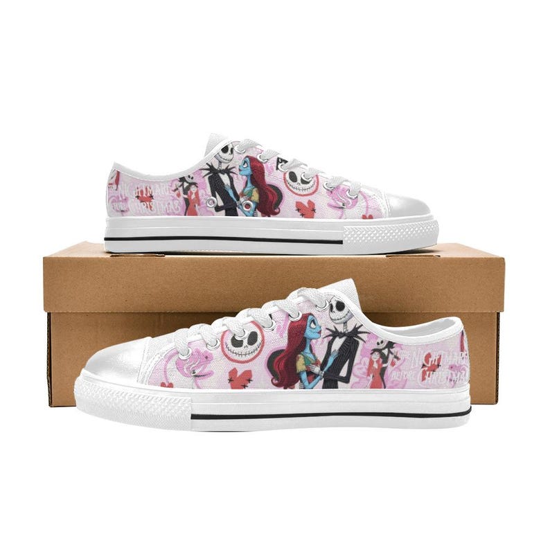 Puede incluir: Zapatillas de lona blancas con un patr&oacute;n repetido de personajes de The Nightmare Before Christmas. Los zapatos de corte bajo tienen cordones blancos, una suela de goma blanca y un fondo rosa.