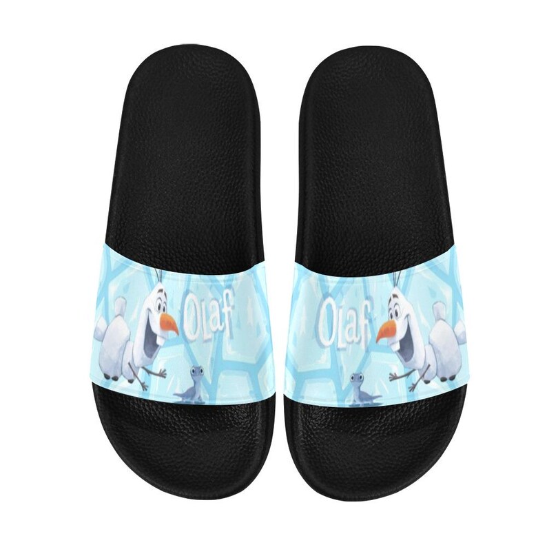 May include: Pair of black slide sandals with a light blue band featuring Olaf from Frozen. The band has a snowflake pattern and the word "Olaf". These sandals are designed for casual wear.