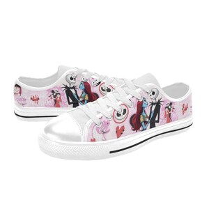 Puede incluir: Zapatillas de lona blancas con un fondo rosa con ilustraciones de personajes de "Pesadilla antes de Navidad". Los zapatos tienen cordones blancos, una puntera blanca y una franja negra a lo largo de la suela.