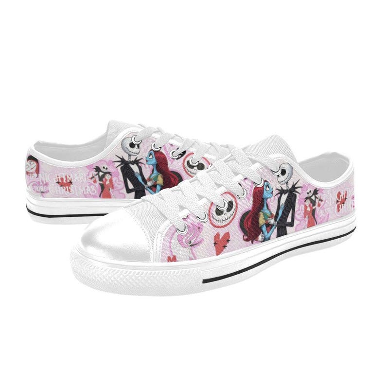 Puede incluir: Zapatillas de lona blancas con un fondo rosa con ilustraciones de personajes de "Pesadilla antes de Navidad". Los zapatos tienen cordones blancos, una puntera blanca y una franja negra a lo largo de la suela.