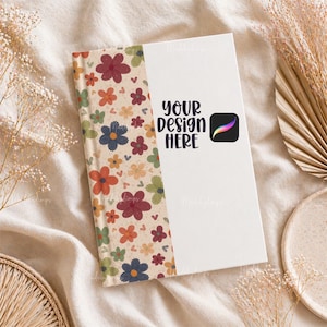 Può includere: Un taccuino bianco con una rilegatura a motivi floreali con fiori rossi, arancioni, blu e verdi. La copertina ha il testo "YOUR DESIGN HERE" e un logo Procreate. Il taccuino è su una superficie beige.