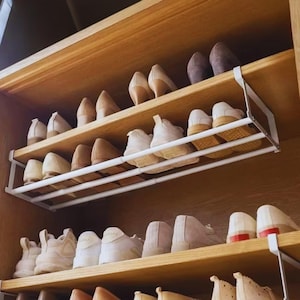 May include: A wooden shoe rack with multiple shelves, filled with various pairs of shoes in neutral colors. A white metal shoe organizer is installed on one shelf. The shoes include sneakers, heels, and flats.