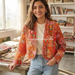 Puede incluir: Una chaqueta acolchada con una base de color naranja vibrante con un estampado floral y botánico multicolor, mangas largas y una abertura frontal recta. La prenda se lleva sobre una camiseta blanca lisa y unos vaqueros azul claro.