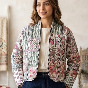 May include: A quilted jacket featuring a white base with a multi-colored floral block print in shades of pink, green, and blue. The jacket has long sleeves, an open front, and is finished with a black and white striped trim along the edges.