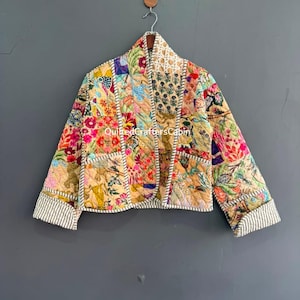 May include: A quilted jacket featuring a patchwork design of various floral and animal prints in shades of yellow, pink, blue, and green. The jacket has long sleeves with striped cuffs, a shawl collar, and visible white stitching along the seams.