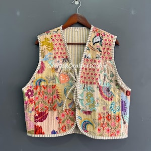 Puede incluir: Un chaleco acolchado con un diseño floral de patchwork en tonos rosa, rojo, azul y amarillo. El chaleco tiene una base color crema con un forro interior a rayas y un ribete blanco. El texto "Quilted Crafters Co" es visible.