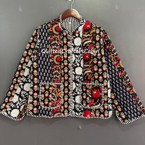 May include: A patchwork quilted jacket with floral and geometric patterns in black, red, white, and gold. The jacket has two pockets and a striped collar. The text "Quilted Crafters Cabin" is visible on the jacket.
