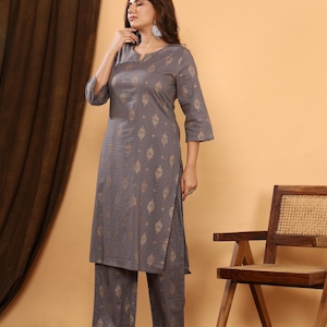 K&ouml;nnte beinhalten: Ein graues Kurta- und Palazzo-Set mit goldenem geometrischem Muster. Das Outfit hat einen V-Ausschnitt und Dreiviertel&auml;rmel. Die Palazzo-Hose hat ein weites Bein. Das Outfit wird mit transparenten Sandalen getragen.