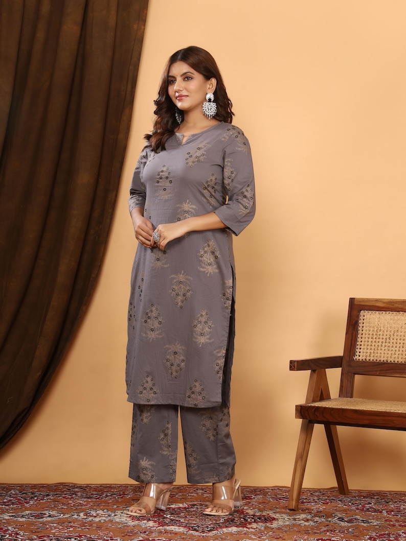 K&ouml;nnte beinhalten: Ein graues Kurta- und passendes Hosen-Set mit floralem Muster. Die Dreiviertel-&Auml;rmel-Kurta hat einen V-Ausschnitt und Seitenschlitze. Die Hose ist weit geschnitten. Das Outfit wird mit transparenten Abs&auml;tzen und silbernen Ohrringen getragen.