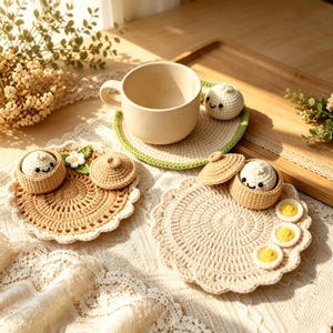 Peut inclure: Trois dessous de verre ronds en crochet avec des bords festonnés. L'un supporte une tasse beige et une petite peluche de ravioli blanc. Un autre présente un panier à raviolis beige, un couvercle et une fleur blanche. Le troisième a un panier.