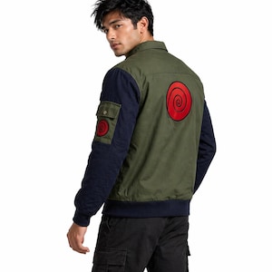 Könnte beinhalten: Olivgrüne und marineblaue Jacke mit rotem Spiraldesign auf dem Rücken und Ärmel. Die Jacke hat eine Knopfleiste, zwei Taschen und einen gerippten Saum. Die Jacke ist aus strapazierfähigem Material gefertigt.