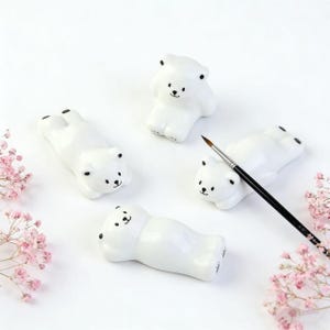 Pode incluir: Uma caneca de cerâmica branca com uma alça preta e o texto "But First, Coffee" em estilo manuscrito. A caneca está sobre uma superfície branca. A caneca tem aproximadamente 10 cm de altura.