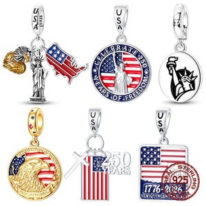 Könnte beinhalten: Eine Sammlung von sechs silber- und goldfarbenen Metallanhängern mit patriotischen amerikanischen Motiven. Die Designs zeigen die Freiheitsstatue, einen Weißkopfseeadler, die Flagge der Vereinigten Staaten und den Text Celebrate 250 Years of Freedom und 1776-2026.