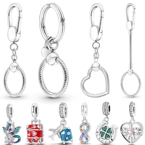 Peut inclure: Collection de breloques et porte-clés argentés. Les breloques comprennent un dragon, une valise rouge, une valise bleue avec un avion, un symbole infini, un fer à cheval avec un trèfle à quatre feuilles et un cœur avec un nœud.