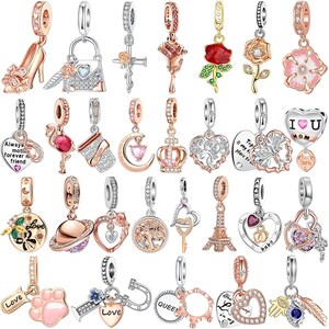 May include: A selection of rose gold and silver charm pendants. Designs include a high-heeled shoe, a lock, a cross, a rose, a flamingo, a coffee cup, a crown, a heart, a paw print, and the Eiffel Tower. Some charms feature gemstones.