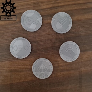 Può includere: Cinque gettoni grigi stampati in 3D con vari simboli e testo. I gettoni sono disposti a cerchio. Ogni gettone ha un design e un testo diversi, tra cui "Engage the Enemy", "Knowing the Enemy", "Dominate the Enemy", "Counter the Enemy" e "Outlast the Enemy."