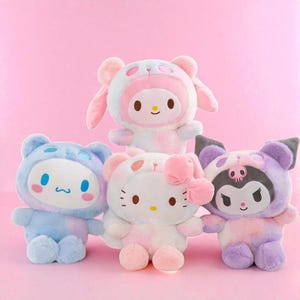 Peut inclure: Quatre peluches aux couleurs pastel, rose, bleu et violet. Chaque jouet a un design de personnage différent, avec de grands yeux et des expressions mignonnes. L'un porte un chapeau de lapin, un autre un nœud.
