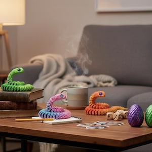 May include: A collection of colorful, articulated snake toys in green, pink, orange, and blue hues, with detailed eyes. Also present are two decorative dragon eggs, dice, and playing cards on a wooden table.