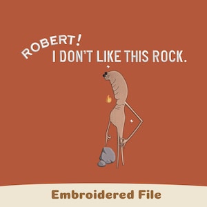 Puede incluir: Archivo bordado con un personaje de dibujos animados y el texto "ROBERT! I DON'T LIKE THIS ROCK." El personaje es de color marrón claro con una pequeña llama y señala una roca gris. El fondo es de color naranja liso.