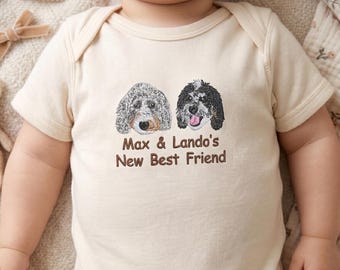 Puede incluir: Body de bebé color crema con un gráfico de dos perros y el texto "Max & Lando's New Best Friend" en marrón. Los perros son un doodle gris y blanco y un doodle negro y blanco. El body tiene mangas cortas.