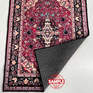 May include: A rectangular rug with a detailed, ornate design in shades of red, black, and cream. The pattern includes floral and geometric elements, with a black border. The rug's underside is a textured gray material. A red "SAMPLE" stamp is visible.