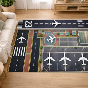 Può includere: Un tappeto rettangolare raffigurante una pista di atterraggio, con superficie nera, segnaletica bianca, il numero 23 e aerei giocattolo. Il design del tappeto include elementi dettagliati dell'aeroporto.
