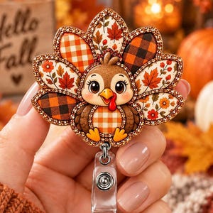 May include: A turkey badge reel featuring a cartoon turkey with large eyes and a red wattle. The turkey's tail feathers are decorated with orange and brown plaid, buffalo check, and autumn leaf patterns, all outlined with a shimmering gold border.