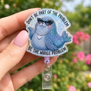 Könnte beinhalten: Ein Ausweishalter mit einem glitzernden blauen Seehund, der eine schwarze Katzenaugen-Sonnenbrille und eine Perlenkette mit Muschelanhänger trägt. Der Text "DON'T BE PART OF THE PROBLEM BE THE WHOLE PROBLEM" ist in schwarzer Schrift abgebildet.
