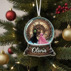 May include: A personalized Christmas ornament featuring a clock face design with two figures inside a snow globe. The ornament has the name "Olivia" on the base and is hanging on a Christmas tree with red and gold ornaments.