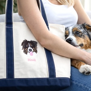 A woman relaxing on a sofa with her dog and a Natural/Navy Bags 8871 personalized tote. The custom embroidered dog face adds a unique touch to this classic canvas boat tote. Search-optimized for personalized pet keepsakes and custom embroidery fashion.