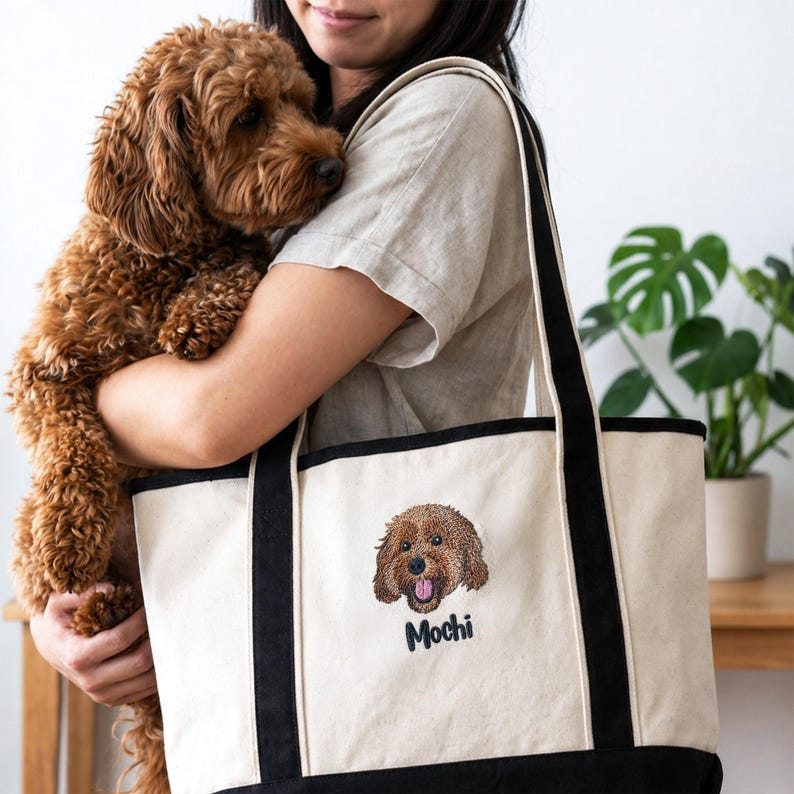 Woman carrying Carmel Classic Cotton Canvas Resort Tote Q125800 while holding curly brown dog. Natural/black canvas tote with straps and custom embroidered pet portrait “Mochi.” Personalized dog mom gift, custom pet embroidery tote bag, durable everyday canvas bag, stylish pet lover accessory.