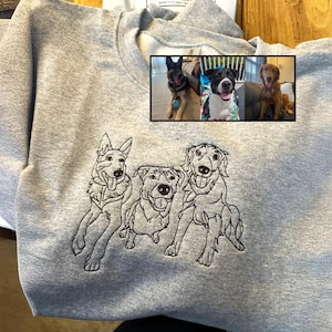 May include: A light gray sweatshirt featuring an embroidered outline of three dogs. Above the embroidery is a framed collage of three color photographs of dogs. The sweatshirt has a crew neck and long sleeves.