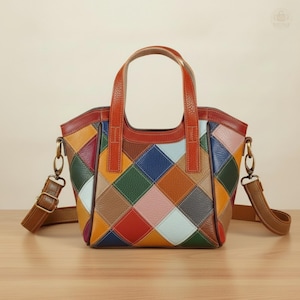 May include: A multi-coloured patchwork leather tote bag with brown handles and a detachable shoulder strap. The bag features a diamond pattern in shades of red, orange, yellow, green, blue, and pink. It is displayed on a wooden surface.