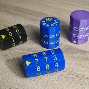 May include: Four colourful, cylindrical dice with rotating number displays. One is black with white numbers, another blue with yellow numbers and the text "HP Count", and a purple die. The fourth die is blue with yellow numbers.