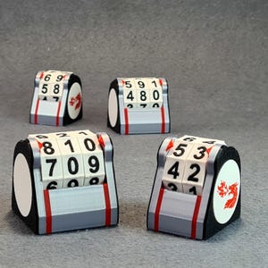 May include: Four dice with rotating number blocks. The dice are black, white, and grey, with red accents and a white circle featuring a red dragon logo. The numbers on the dice are black.