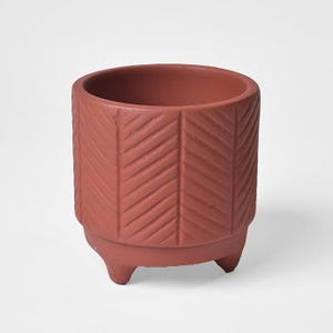 May include: A terracotta-colored planter with a textured chevron pattern. The small, round pot sits on three short legs. The top opening is circular, and the pot is suitable for small plants.