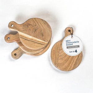 May include: Set of four mini charcuterie boards. Each board is made of light brown wood with a handle and a 5-inch diameter. The boards are round with a natural wood grain pattern. A tag reads "Mini Charcuterie Board" and "Set of 4".