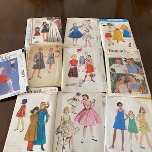 Op de afbeelding: Een verzameling van tien vintage naaipatronen van merken zoals McCall's, Simplicity en Butterick. Elke papieren envelop bevat gedrukte illustraties van verschillende kledingstijlen, waaronder jurken, rokken en tops, met merknamen en patroonnummers zichtbaar op de voorzijde.