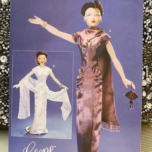 May include: A Vogue Craft pattern featuring a doll in a long, shimmering, plum-colored gown with a matching shawl and a small purse. The pattern includes a second doll in a white gown. The text "Gene" is visible.