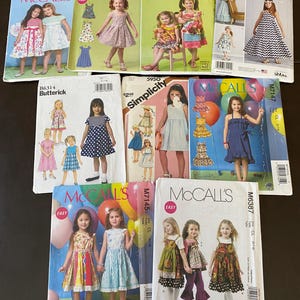 May include: A collection of children's dress sewing patterns from McCall's, Butterick, and Simplicity. The patterns feature colorful illustrations of girls wearing various dress styles. The patterns are labeled with numbers and brand names.