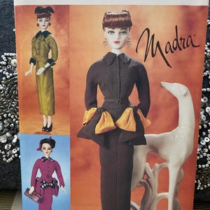 May include: Vogue Doll Collection pattern featuring three doll illustrations. The pattern number is 7382, and it is one size. The dolls are dressed in stylish outfits, including a long olive green dress, a dark brown dress with orange accents, and a pink suit.