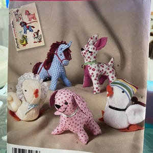 May include: A Simplicity sewing pattern envelope 2763 for stuffed toys. The front displays five fabric animal figures: a blue gingham horse, a cherry-print dog, a pink patterned puppy, a white chick with a lace bonnet, and a white duck with a striped hat.