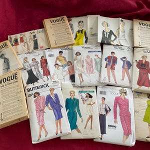 May include: A collection of vintage sewing pattern envelopes from brands including Vogue and Butterick. The paper envelopes feature various illustrations of clothing designs, including dresses, skirts, and tops, with printed text and instructional guides.