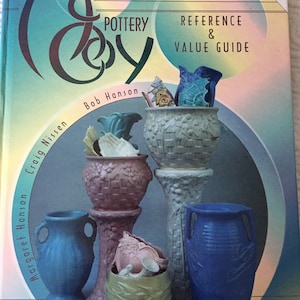 May include: A book titled "McCoy Pottery Collector's Reference & Value Guide" with an updated values section. The cover features a colorful image of McCoy pottery pieces, including a blue vase, a green bowl, and a pink and white bowl.