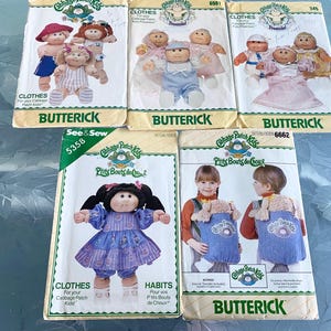 May include: Five vintage Butterick sewing patterns for Cabbage Patch Kids clothes and accessories. The patterns feature illustrations of the dolls in various outfits, including dresses and overalls. The patterns are labelled with numbers and include the "See & Sew" logo.