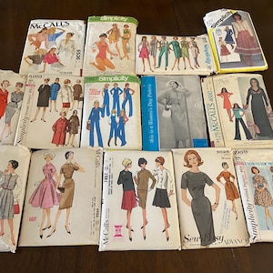 Może przedstawiać: Kolekcja czternastu zabytkowych wykrojów krawieckich marek takich jak Simplicity, McCall's i Advance. Każda papierowa koperta zawiera ilustracje różnych stylów odzieży, w tym sukienek, spódnic, bluzek i spodni, wraz z nadrukowanym tekstem.