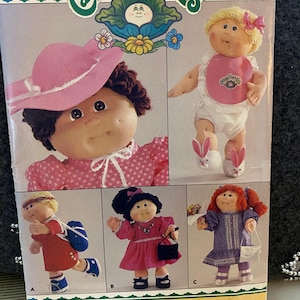 May include: A vintage Cabbage Patch Kids pattern envelope featuring illustrations of several dolls in various outfits. The envelope has the text "Cabbage Patch Kids" and "Butterick" printed on it. The dolls are wearing dresses, hats, and carrying accessories.