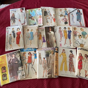 May include: A collection of sixteen vintage sewing patterns from brands including Simplicity, McCall's, and Butterick. Each paper envelope features illustrations of various garments such as dresses, coats, and pants, with printed brand names and pattern numbers.